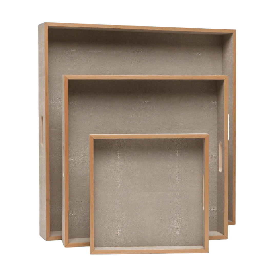 Three empty, square Amina Square Tray Sand serving trays by Made Goods, each with raised edges and elegant wood trim, are stacked upright against a white background.