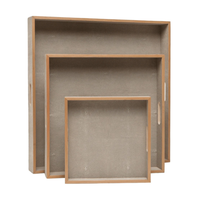 Three empty, square Amina Square Tray Sand serving trays by Made Goods, each with raised edges and elegant wood trim, are stacked upright against a white background.