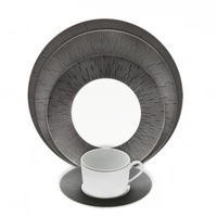 A modern Haviland Anthracite Infini Dinnerware Grey set features a white cup and saucer alongside two round plates with a dark gray, finely lined radial pattern. Made from Limoges porcelain, it stands out against the white background.