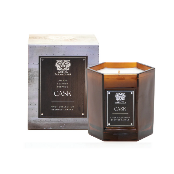 A brown hexagonal glass Cask Candle from Antica Farmacista/Harper sits before its box. It features a tobacco scent and is crafted with a premium soy-paraffin wax blend.