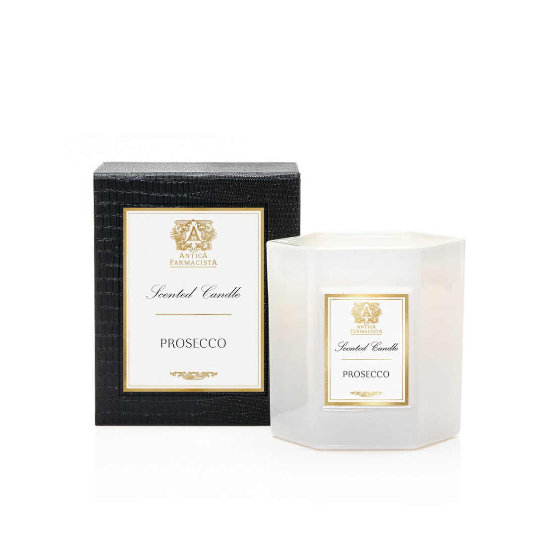 A white hexagonal Prosecco Candle by Antica Farmacista/Harper sits beside its black textured box, both adorned with gold and white labels. Made from a soy-paraffin wax blend for a refined scent experience.