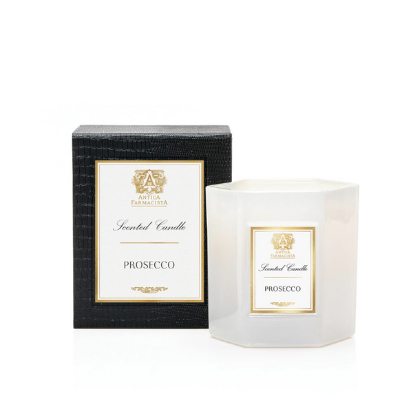 A white hexagonal Prosecco Candle by Antica Farmacista/Harper sits beside its black textured box, both adorned with gold and white labels. Made from a soy-paraffin wax blend for a refined scent experience.