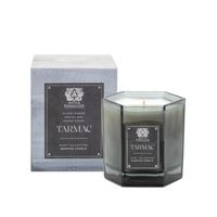 A gray octagonal glass Tarmac Candle by Antica Farmacista/Harper sits before its matching box, both with black and silver labels highlighting scents of silver woods, earthy oak, and green cedar.