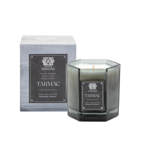 A gray octagonal glass Tarmac Candle by Antica Farmacista/Harper sits before its matching box, both with black and silver labels highlighting scents of silver woods, earthy oak, and green cedar.