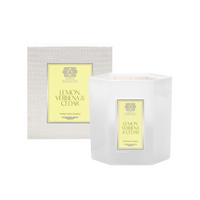 A white hexagonal Antica Farmacista/Harper Lemon Verbena & Cedar Candle sits before a matching textured box with a yellow label displaying the scent name and decorative emblem.