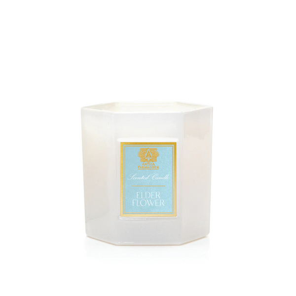 A white hexagonal botanical candle jar from Antica Farmacista/Harper features a light blue label reading "Scented Candle" and "Elderflower Candle." This unlit product sits against a plain white background.