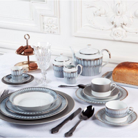 A formal table features Arcades Platinum Dinnerware by Philippe Deshoulieres BIA, crystal glasses, a loaf of bread, and a tray of chocolate macarons on a white tablecloth in an elegantly decorated room.