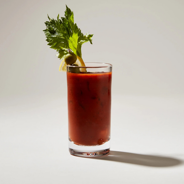 A Bloody Mary, garnished with celery, olive, and lemon, served in the elegantly handblown Simon Pearce Ascutney Tumbler—barware designed for perfect presentation against a light background.