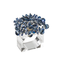 The Kim Seybert Aster Napkin Ring Set of 4 features a modern, clear thick band topped with a spiky cluster of large faceted blue gemstones, making it a stunning statement piece for your table decor.