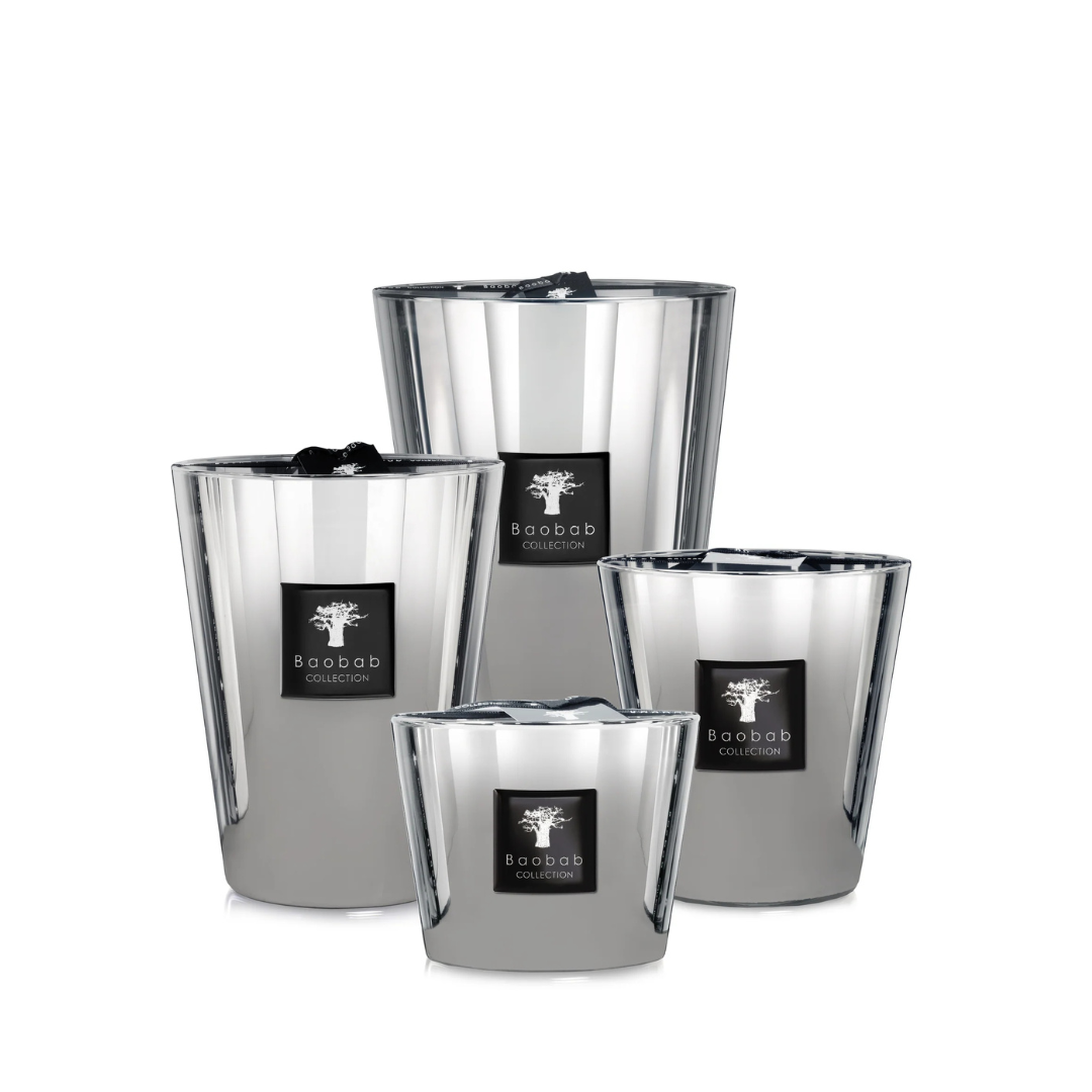 Four reflective silver candles of varying heights from Baobab’s Les Exclusives Platinum collection, each with a black branded label, are arranged together on a white background to create a warm and inviting atmosphere.