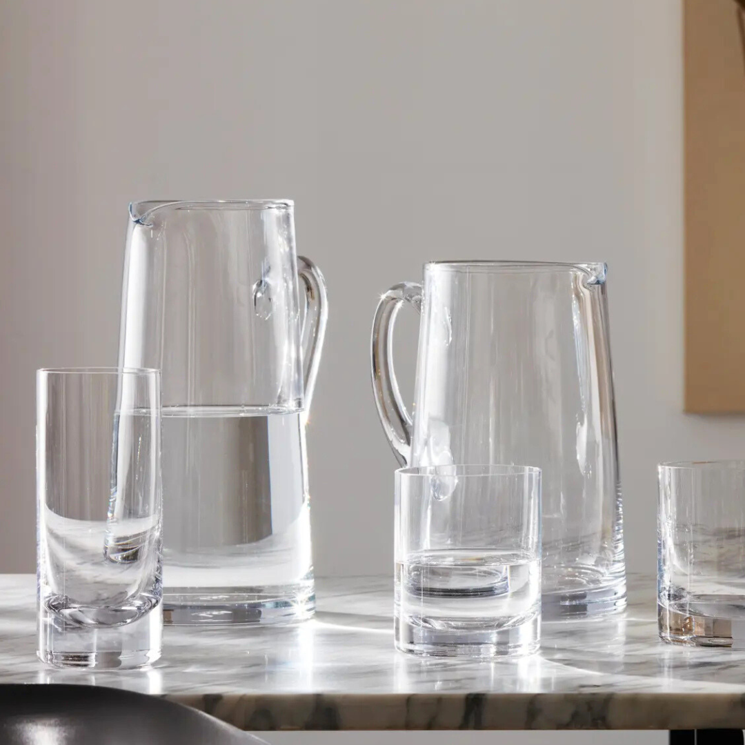 LSA's Bar Tapered Pitcher, a clear glass jug filled with water, is displayed with matching tumblers on a marble surface in soft natural light against a plain background.