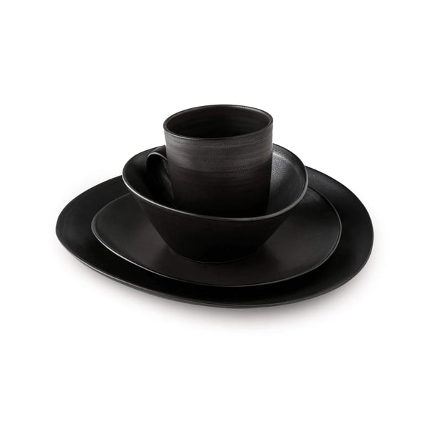 A stack of Simon Pearce Barre Dinnerware Slate stoneware dishes with a matching mug, all in matte black, from the modern dinnerware set, displayed on a white background.