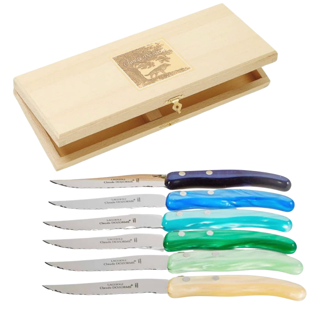 The Claude Dozorme Berlingot Blue & Green Steak Knives Set of 6 features stainless steel blades and colorful handles, beautifully arranged below an open wooden box. These expertly crafted French knives add style to any table.