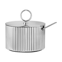 The Georg Jensen Bernadotte Sugar Bowl in stainless steel features a ribbed Scandinavian design, a lid with a round handle, and comes with a matching spoon that fits neatly into a side slot.