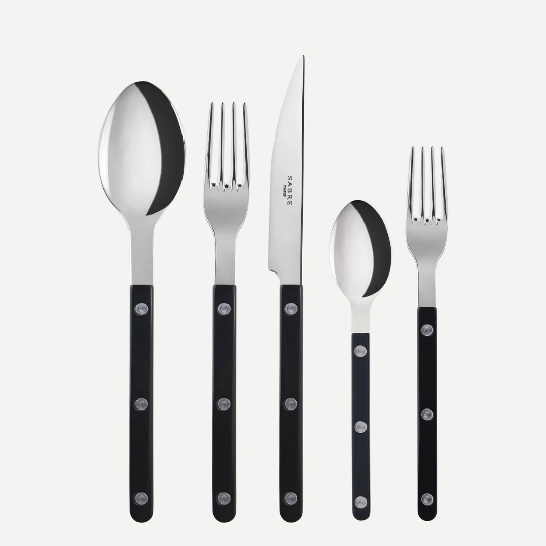 The Sabre Bistrot Solid Flatware 5 Piece Setting - Shiny includes a tablespoon, dinner fork, knife, teaspoon, and salad fork with black handles, shown upright on a white background. Paris-inspired design from the Bistrot collection.