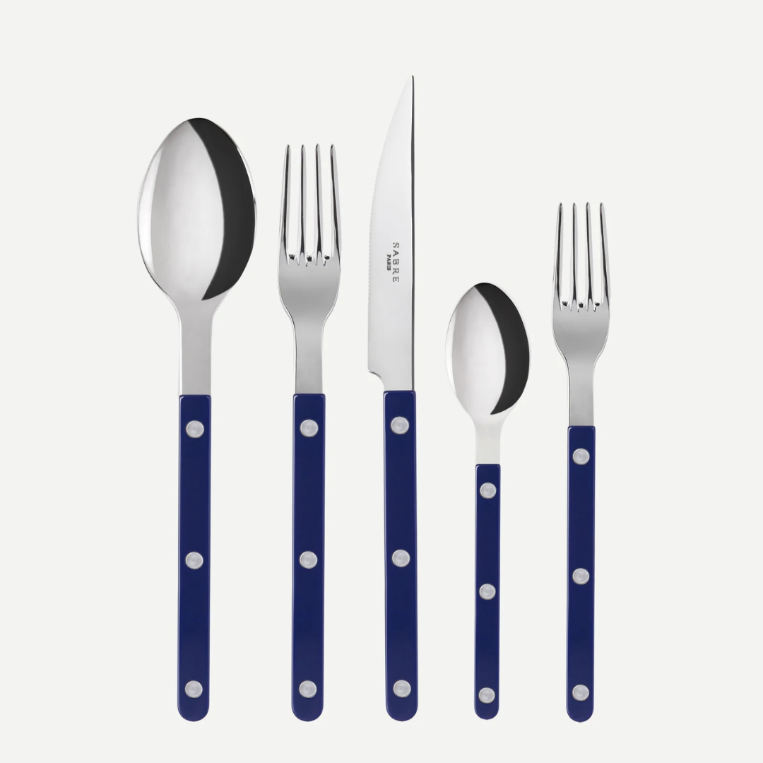 The Sabre Bistrot Solid Flatware 5 Piece Setting - Shiny features dark blue handles with three silver rivets and includes a tablespoon, dinner knife, dinner fork, teaspoon, and salad fork, all shown upright on a white background.