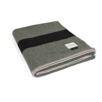 The Siempre Recycled Alpaca Throw by Blacksaw is a heavyweight grey wool blanket with a bold black stripe, white stitched edges, and a rectangular label—a perfect recycled fireside companion.
