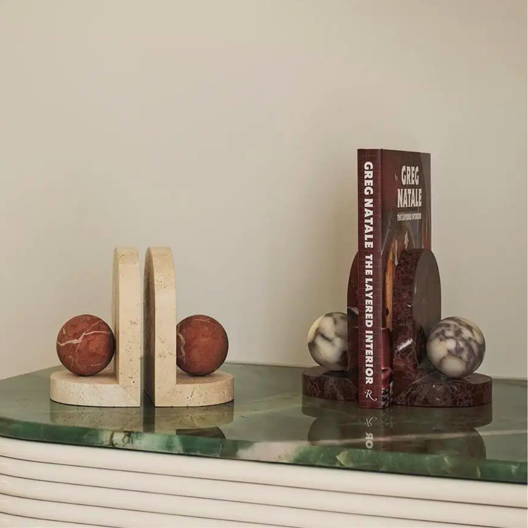 The Blitz Marble Bookend Set - Merlot by Greg Natale features two marble bookends with red or white stone spheres, elegantly displaying Greg Natale: The Layered Interior on a green marble surface—perfect for any modern space.