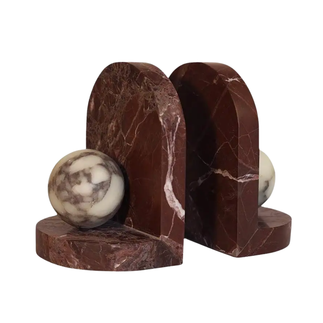 The Greg Natale Blitz Marble Bookend Set - Merlot features two dark brown marble bookends with arched tops and white-dark marbled spheres atop natural veining, perfect for elevating any contemporary space. Plain white background.