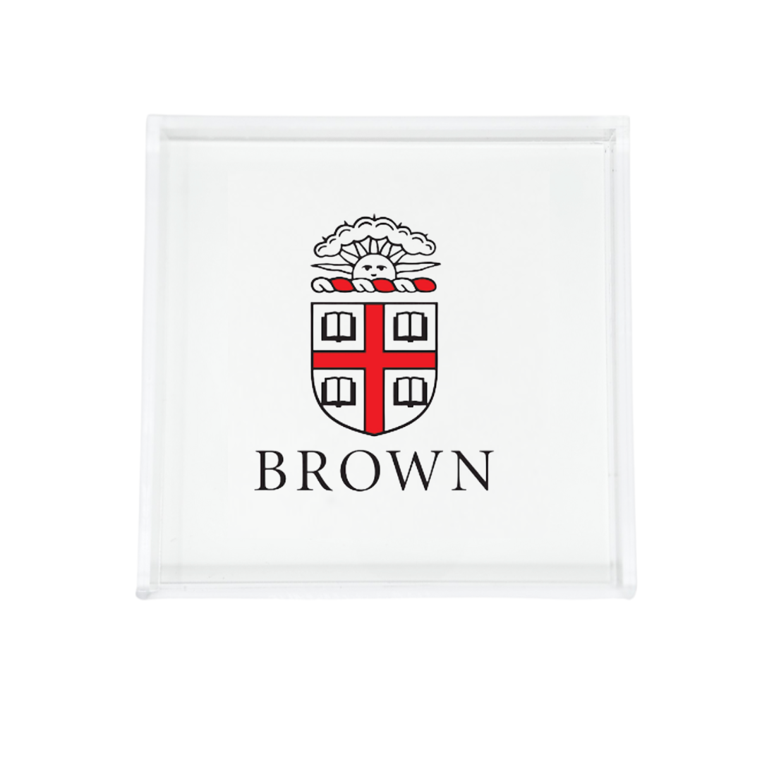 The Eye Candy College Acrylic Catchall Tray displays the Brown University coat of arms with a red cross, four open books, and "BROWN" below—a stylish and practical dorm room accessory.