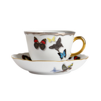 A white porcelain teacup and saucer with a gold handle, adorned with colorful butterflies, from Vista Alegre's Butterfly Parade Dinnerware, adds a touch of luxury and elegance to your table.