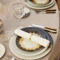 Elegant setting featuring Marie Daâge Cercle d'Ecailles Dessert Plate, gray accent plate, gold-handled cutlery, crisp white napkin in a gold ring, wine and water glasses on a textured beige tablecloth.