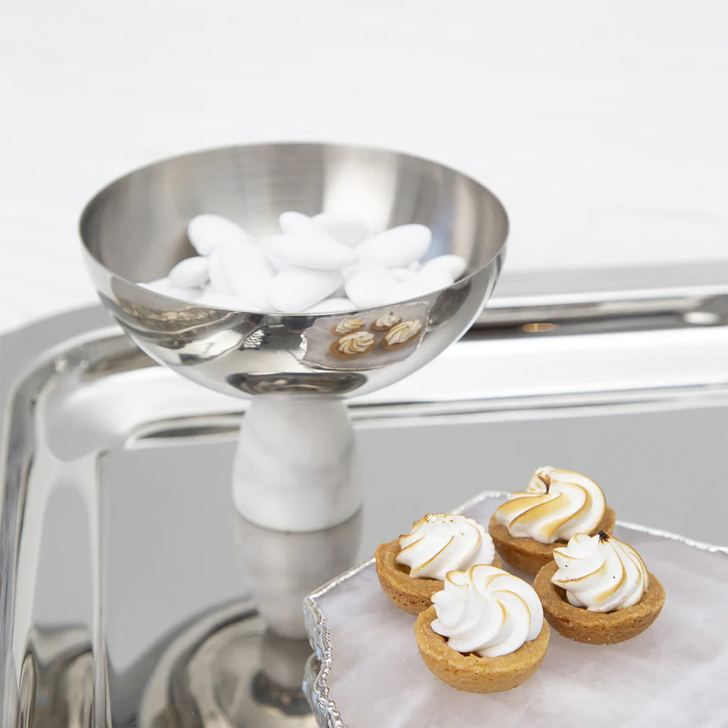 An Anna New York Coluna Carrara Marble Nut Bowl filled with white candy-coated almonds sits on a tray next to three mini tartlets topped with swirled meringue.