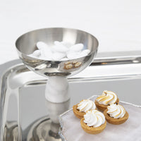 An Anna New York Coluna Carrara Marble Nut Bowl filled with white candy-coated almonds sits on a tray next to three mini tartlets topped with swirled meringue.