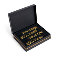 A luxury gift box with a gold trim, open to reveal four Spirale Gold Cocktail Forks by L'Objet, each featuring elegant wavy and spiral designs, neatly arranged on a black foam insert.