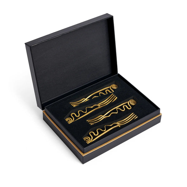A luxury gift box with a gold trim, open to reveal four Spirale Gold Cocktail Forks by L'Objet, each featuring elegant wavy and spiral designs, neatly arranged on a black foam insert.