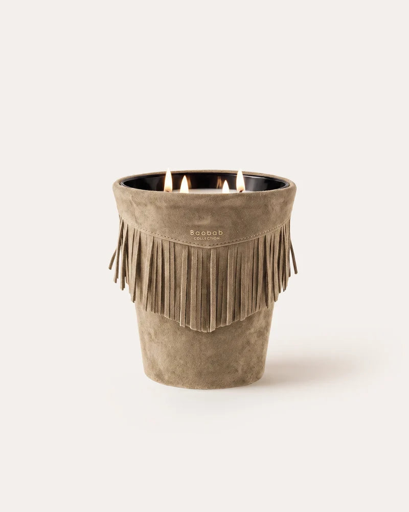 A lit three-wick Baobab Calamity Jane Candle - The Plains in a mineral taupe leather, tan, fringe-trimmed suede vessel.