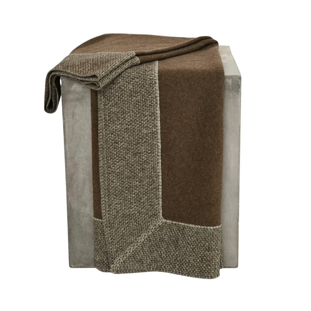 The Chuluu Yak Down Throw in Chocolate by Hangai Mountain Textiles, a hypoallergenic blanket crafted from lightweight jersey knit, is folded and draped over a rectangular concrete block, with part of the throw hanging down the side.