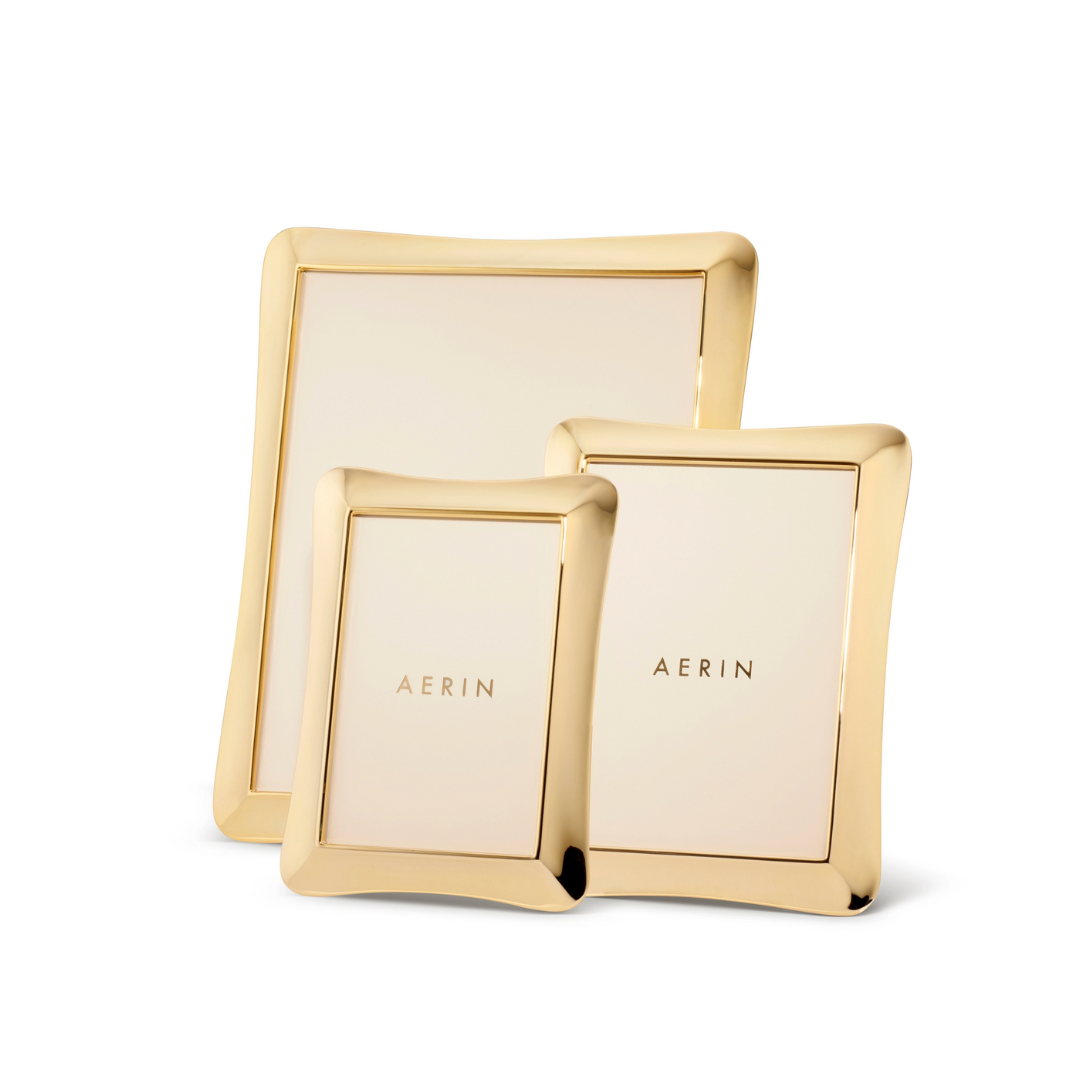 Three Cecile Frames from Aerin, each in a different size and featuring smooth, gently curved gold edges, are arranged together on a white background. Their three-dimensional design adds subtle depth, while each center is adorned with the AERIN logo in gold lettering—an elegant touch for any feminine desk frame collection.