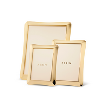 Three Cecile Frames from Aerin, each in a different size and featuring smooth, gently curved gold edges, are arranged together on a white background. Their three-dimensional design adds subtle depth, while each center is adorned with the AERIN logo in gold lettering—an elegant touch for any feminine desk frame collection.
