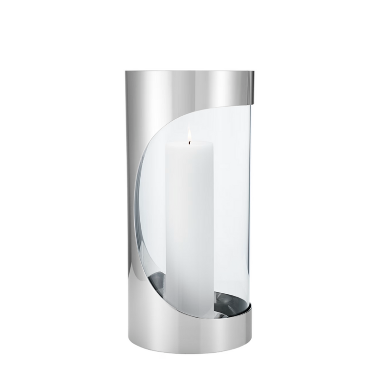 A lit white pillar candle glows inside the Georg Jensen Chrome Contours Hurricane 13", a modern cylindrical holder with silver accents and an open front—ideal for stylish, contemporary home lighting.