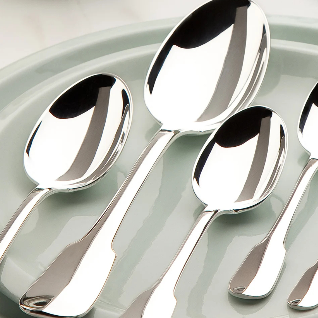 Five polished silver-plated spoons from the Christofle Cluny Flatware 5 Piece Setting are laid out on a light gray plate, their reflective surfaces gleaming against a white background.