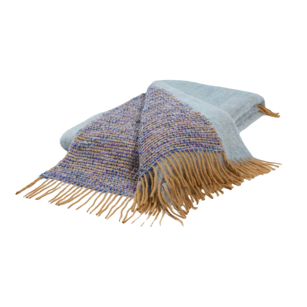 The Coco Throw by Mantas Ezcaray is a folded, double-sided blanket with light blue and multicolored sections and tan fringe on the edges, displayed on a white background.