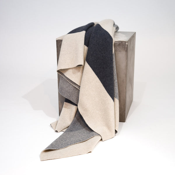 A Color Field Charcoal & Stone Grey Cashmere Throw by Hangai Mountain Textiles in charcoal and light grey color-blocked cashmere draped over a square block.