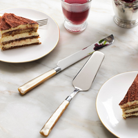 Two plates with slices of layered cake, a glass of red liquid, and the Blue Pheasant Colson Cake Serving Set with cream handles rest on a marble surface.