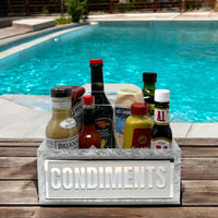 The Eye Candy Porter Acrylic Condiments Caddy organizes bottles of sauces and dressings on a wooden table by a bright blue pool.