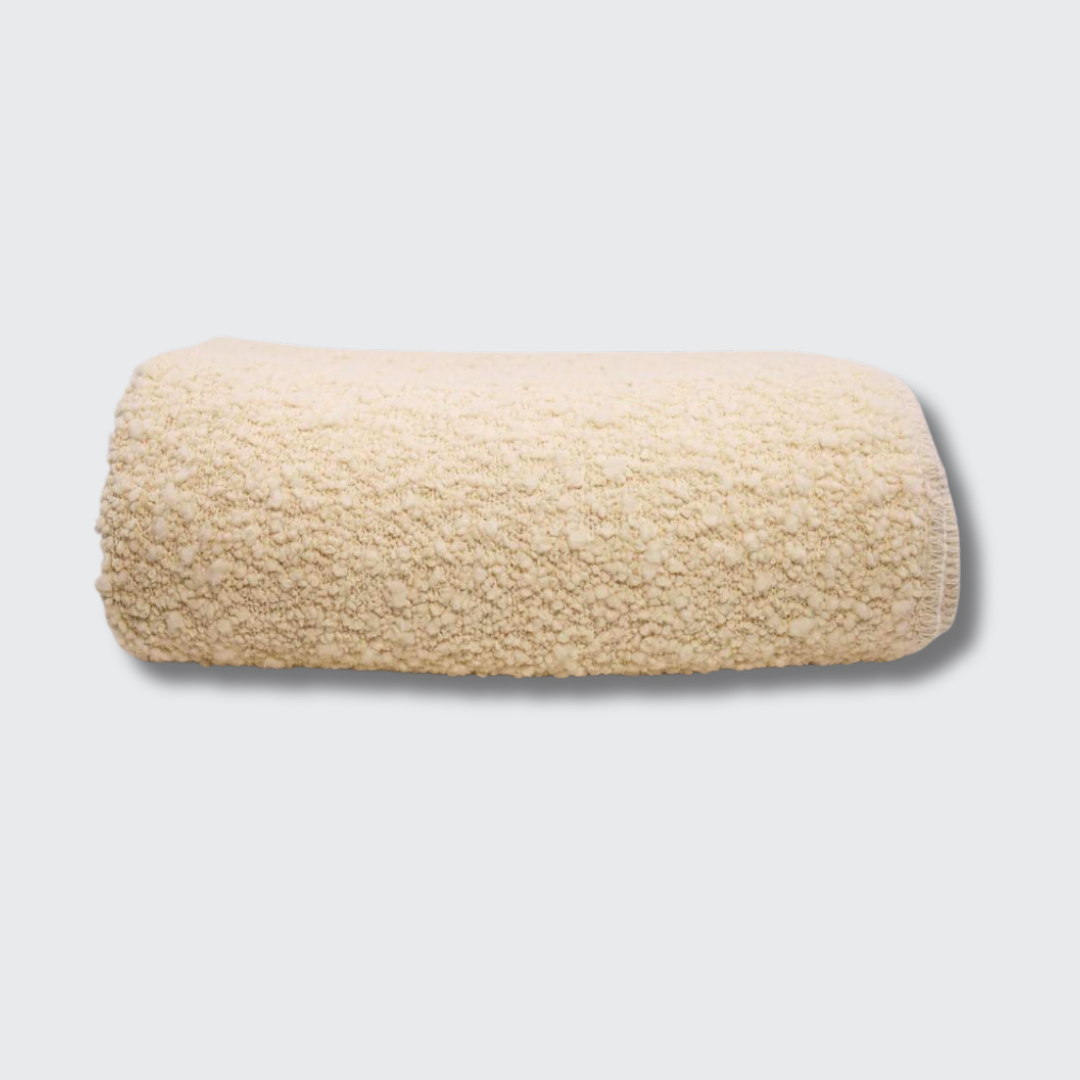 The Uniquity Kusama Boucle Cream Throw, featuring a textured cream weave, is neatly folded and displayed against a plain light gray background.