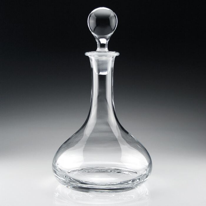 The William Yeoward Classic Ships Decanter, crafted from handmade crystal glass with a round stopper, features a wide base and narrow neck, elegantly displayed on a reflective surface against a dark gradient background.