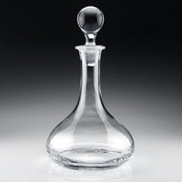 The William Yeoward Classic Ships Decanter, crafted from handmade crystal glass with a round stopper, features a wide base and narrow neck, elegantly displayed on a reflective surface against a dark gradient background.