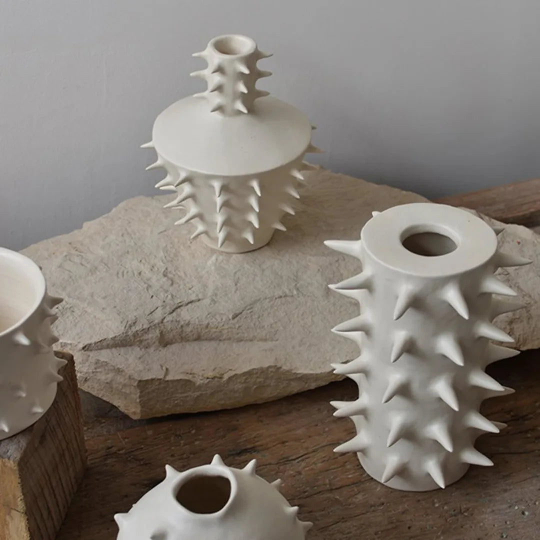 Three “Spikes Vase III - White” vases by OWO Ceramics, each featuring striking sculptural spikes, are displayed on rustic stone and wood surfaces against a simple gray background, creating truly unique home decor.