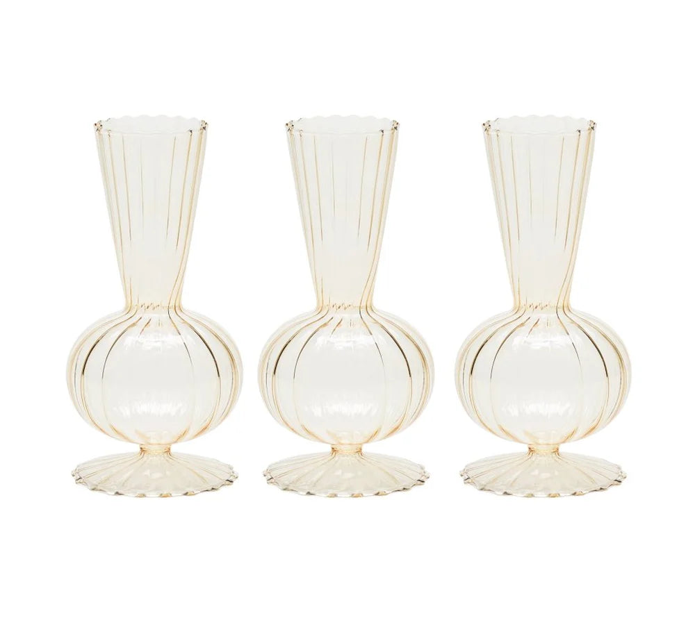 The Kim Seybert Tess Bud Vase Set of 4 in Champagne features identical translucent vases with round bases, fluted bottoms, narrow necks, and vertical ribbed lines, arranged side by side on a white background.