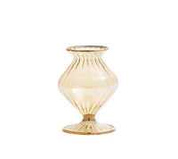The Kim Seybert Champagne Rib Gold Detail Vase is a translucent, amber mouth-blown glass piece with iridescent luster, flared lip, ribbed texture, and wide round base. Its curvy hourglass silhouette stands out against a plain white background.