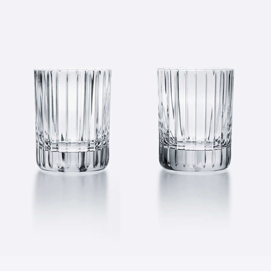 Two clear Baccarat Harmonie Barware glasses by Baccarat, featuring an elegant faceted design, are placed side by side on a white background with subtle reflections beneath them.