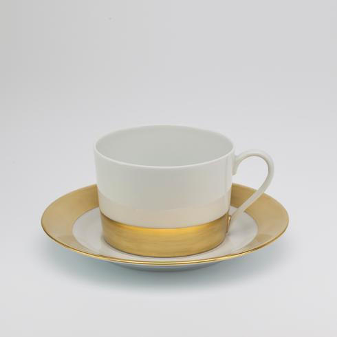 The Danielle Gold Dinnerware teacup by Royal Limoges features white porcelain with a gold band near the base and comes with a matching saucer adorned with a gold rim, shown on a plain light gray background.