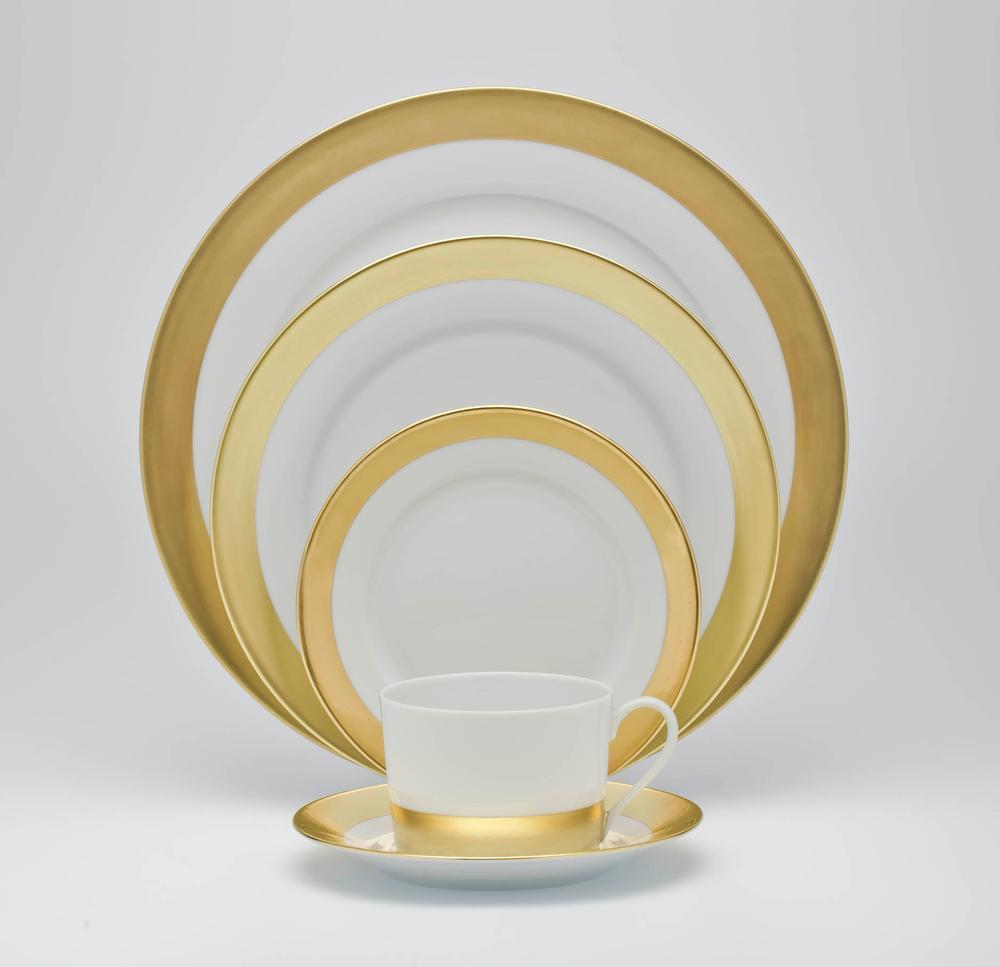 The Royal Limoges Danielle Gold Dinnerware set, featuring gold-banded porcelain pieces—dinner plate, salad plate, bread plate, soup bowl, cup, and saucer—is arranged in a neat overlapping display on a plain white background.