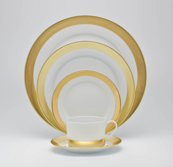 The Royal Limoges Danielle Gold Dinnerware set, featuring gold-banded porcelain pieces—dinner plate, salad plate, bread plate, soup bowl, cup, and saucer—is arranged in a neat overlapping display on a plain white background.